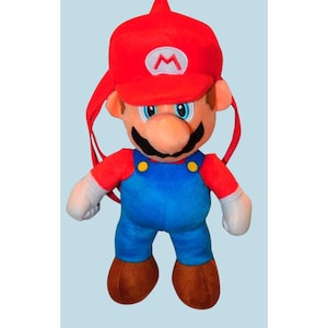 May include: A plush toy of the video game character Mario. The toy has a red hat with a white "M" emblem, a red shirt, blue overalls, and brown shoes. The toy has a black mustache and a large nose. The toy is designed to be worn as a backpack.