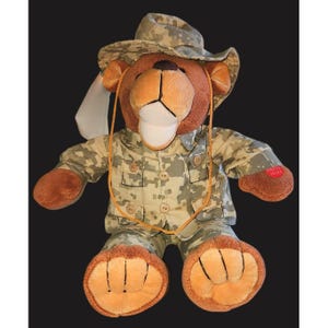 May include: A brown teddy bear wearing a camouflage hat and uniform. The plush toy has a white muzzle, tan paws, and a button-down shirt. The bear has a tan rope around its neck and the words "PRESS HERE" on its paw.