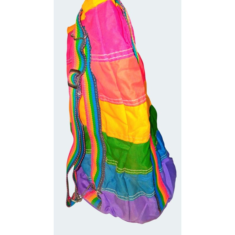 May include: A colorful backpack with a rainbow strap and a patchwork design. The bag features panels of pink, orange, yellow, green, blue, and purple. The straps are rainbow-striped with silver metal hardware.