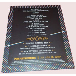 May include: The back cover of the Pink Floyd The Dark Side of the Moon album features a black background with a white tracklist, Dolby Atmos logo, and technical audio specifications. A yellow waveform graphic sits above the mix details.