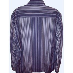 May include: A long-sleeved button-down shirt featuring a vertical striped pattern in various shades of purple, lavender, and white. The shirt has a standard collar and a back yoke, with the stripes running vertically down the body and sleeves.