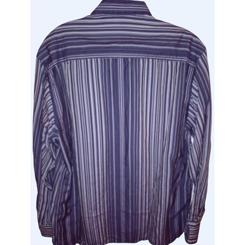 May include: A long-sleeved button-down shirt featuring a vertical striped pattern in various shades of purple, lavender, and white. The shirt has a standard collar and a back yoke, with the stripes running vertically down the body and sleeves.