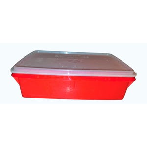 May include: A rectangular red plastic food storage container with a clear lid. The container has a slightly curved design and a white rim. The lid appears to be made of a translucent plastic.