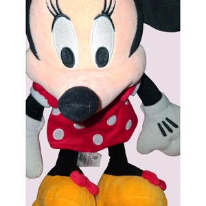May include: A plush Minnie Mouse doll. The doll has a pink face, black ears, and a black nose. She wears a red dress with white polka dots, white gloves, and yellow shoes with red bows. The doll is a popular character.