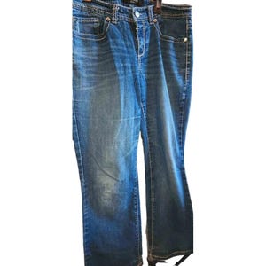 May include: Blue denim jeans with a classic five-pocket design. The jeans feature white stitching and a button and zipper closure. The jeans are hanging on a black hanger.