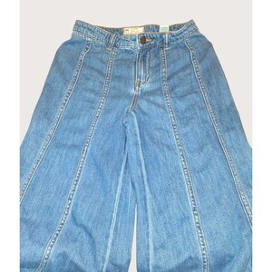 May include: Pale blue denim trousers with a wide leg cut. The trousers have a button and zip fastening, with vertical seams creating a panelled effect. The fabric has a faded wash, giving it a vintage appearance.
