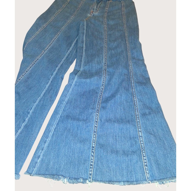 May include: Light blue denim jeans with a flared leg design. The jeans have a high waist and feature vertical seams down the front and back of the legs. The hemline is frayed.