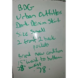 Pode incluir: Quadro branco com texto manuscrito verde. O texto diz: "BDG Urban Outfitters Dark Denim Skirt Tamanho Small 2 bolsos frontais 2 traseiros Condi&ccedil;&atilde;o nova 15" cintura &agrave; bainha (38 cm) 28" cintura (71 cm) .78."