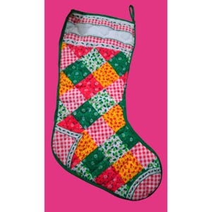 May include: A quilted Christmas stocking with a patchwork design. The stocking features red, green, and yellow squares, with a white top and a green trim. The pattern includes gingham and floral prints. A green loop is at the top for hanging.