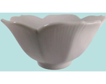 May include: A white ceramic bowl with a scalloped, petal-like rim and a smooth, glossy finish. The bowl features vertical fluted detailing along the exterior sides, tapering down to a circular base, creating a flower-like silhouette.