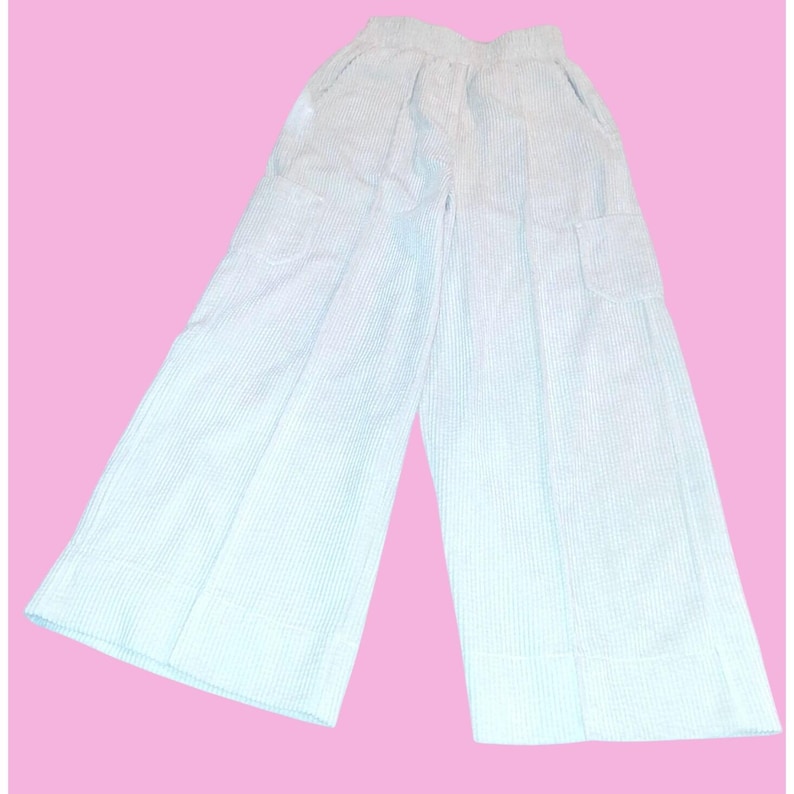 May include: White and light blue striped wide-leg pants with pockets. The pants have a high waist and a relaxed fit, perfect for casual wear. The fabric appears to be lightweight and breathable, suitable for warmer weather.