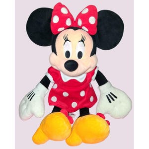 May include: A plush Minnie Mouse doll. The doll has black ears, a red dress with white polka dots, and a matching bow. Her gloves are white, and her shoes are yellow.