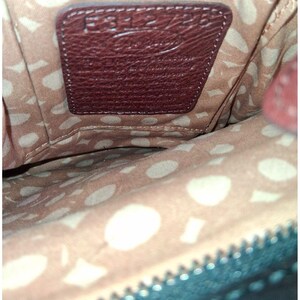 Puede incluir: El interior de un bolso con forro color canela y un patr&oacute;n abstracto repetitivo en color crema. Un parche de cuero marr&oacute;n oscuro est&aacute; cosido al forro, grabado con el texto E312725 y un logotipo de marca, con una textura granulada visible.