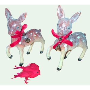 May include: Two vintage-style deer ornaments with red velvet bows and small bells. The deer are brown with white spots and glitter. A small red bird ornament is also present.