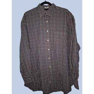 May include: A long-sleeved button-down shirt with a checkered pattern in navy, red, and cream. The shirt has a classic collar, a chest pocket, and buttoned cuffs. It is hanging on a black hanger against a light blue background.