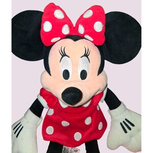 May include: A plush Minnie Mouse doll featuring a red dress and bow with white polka dots. The doll has black ears, a pink face, and white gloves. The doll is a classic Disney character.