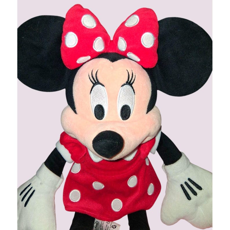 May include: A plush Minnie Mouse doll featuring a red dress and bow with white polka dots. The doll has black ears, a pink face, and white gloves. The doll is a classic Disney character.