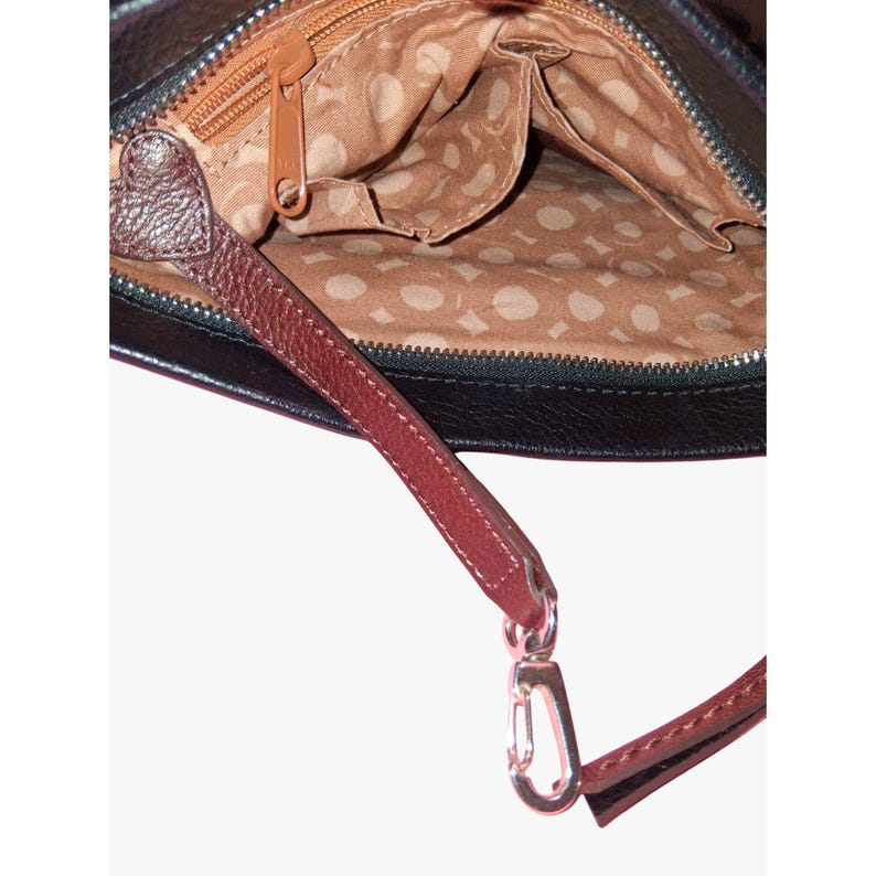 Puede incluir: Un bolso negro con exterior texturizado y forro interior color canela con un patr&oacute;n circular repetitivo. El bolso incluye una correa de cuero marr&oacute;n con un detalle en forma de coraz&oacute;n y un cierre de mosquet&oacute;n de metal plateado.