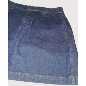 Pode incluir: Saia jeans azul escuro com costuras laranja-castanho vis&iacute;veis. A saia tem um design cl&aacute;ssico de cinco bolsos e uma bainha reta. O tecido parece ser um denim de peso m&eacute;dio.