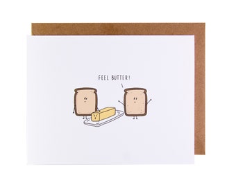 May include: A white card with a brown envelope. The card has a cartoon illustration of two slices of bread with faces and a stick of butter with a face. The text on the card reads "Feel Butter!"