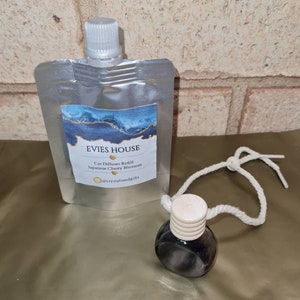 May include: A clear plastic pouch with a white cap and a label that reads "Evies House Car Diffuser Refill Japanese Cherry Blossom @crystalsandgifts". A small glass bottle with a white cap and a white string is attached to the pouch.