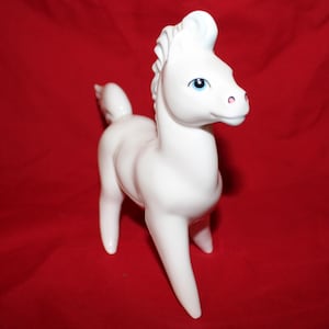 May include: A white ceramic horse figurine with blue eyes and a pink nose. The horse is standing on all four legs and has a long tail.