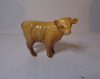 May include: A small, ceramic figurine of a brown calf. The calf is standing on all four legs and has a light brown coat.