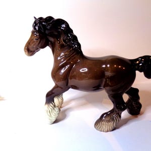 Op de afbeelding: Een bruin en zwart keramiek paardbeeldje met witte hoeven. Het paard staat op alle vier de poten en heeft een lange manen en staart.