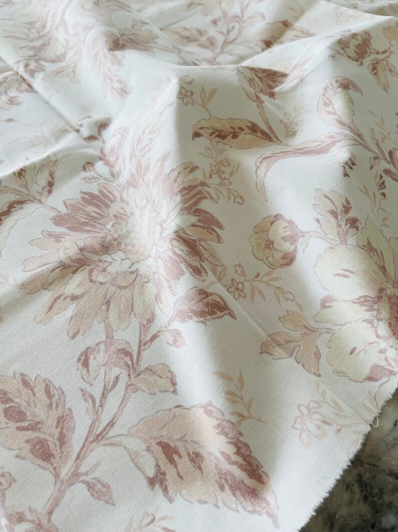 May include: White fabric with a floral pattern in shades of brown and beige. The fabric has a soft, textured feel.