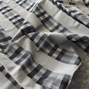 Könnte beinhalten: Ein weißer Stoff mit einem schwarzen und grauen Karomuster. Der Stoff ist gefaltet und zerknittert, wodurch ein strukturierter Look entsteht.