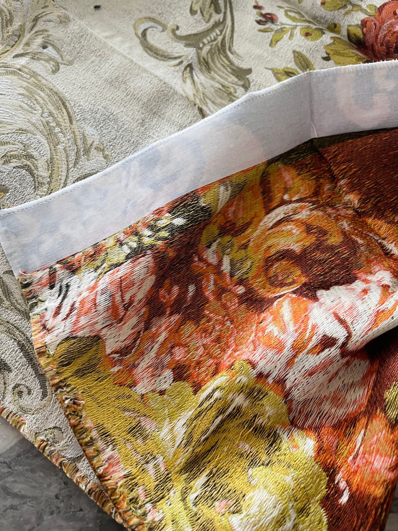 May include: Close-up of a fabric with a floral pattern in shades of orange, yellow, and brown. The fabric has a textured surface and a white border.