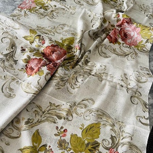 May include: A white fabric with a floral pattern. The fabric features a repeating pattern of pink and red roses with green leaves and stems. The background is a light beige color with a subtle texture.