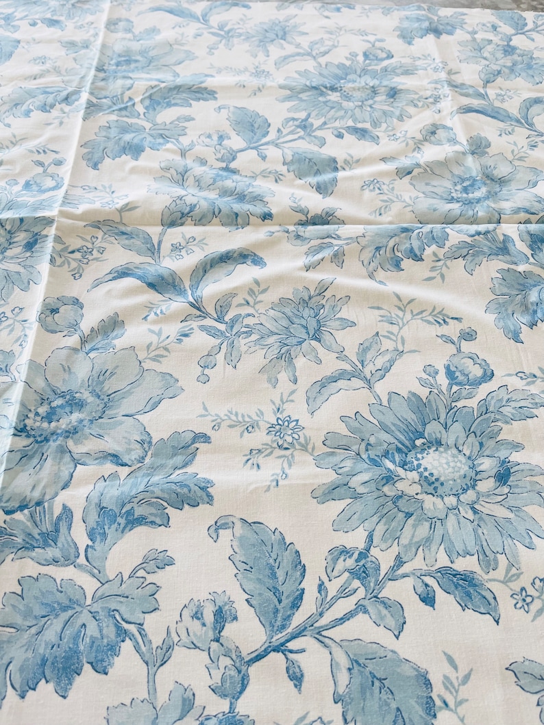 May include: White fabric with a blue floral pattern. The pattern features large blue flowers with intricate details and leaves.