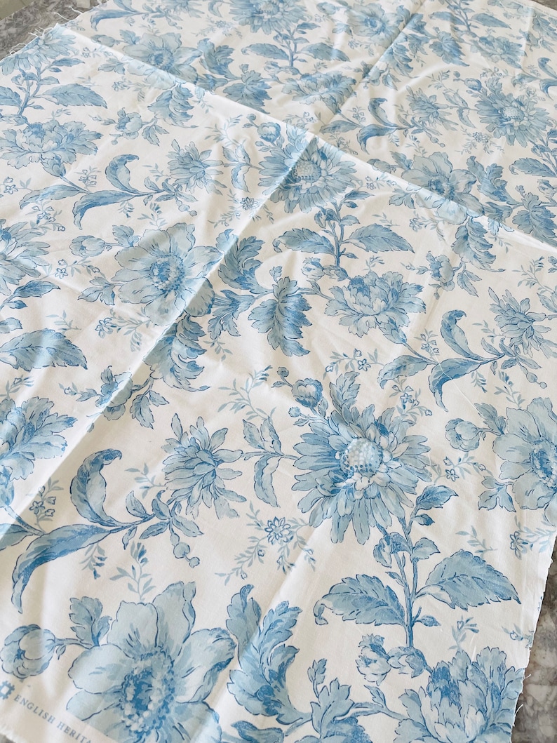 May include: Blue and white floral fabric with a repeating pattern of large and small flowers. The fabric has a vintage feel and would be perfect for upholstery or curtains.