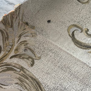 May include: Close-up of a beige fabric with a gold and brown floral pattern. The fabric has a textured surface and appears to be woven.