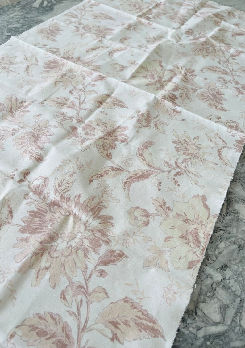 May include: White fabric with a floral pattern in shades of brown and beige. The fabric has a subtle texture and a slightly distressed look.