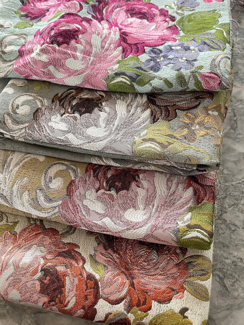 May include: A stack of five fabric swatches with floral patterns. The fabrics are in shades of pink, green, brown, and white. The patterns are intricate and detailed, featuring roses, leaves, and other floral elements.