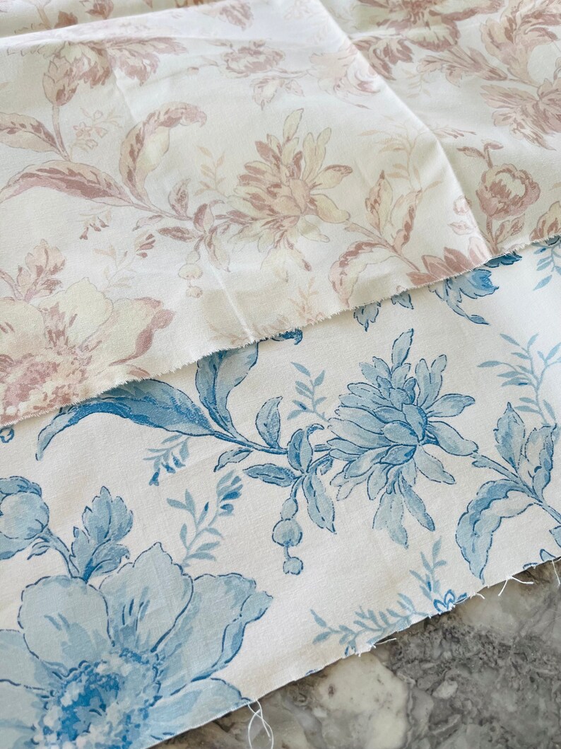May include: Two pieces of fabric with floral patterns. The top fabric is white with a pink floral pattern. The bottom fabric is white with a blue floral pattern.