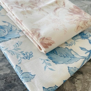May include: Two pieces of white fabric with floral patterns. One fabric has a light pink floral pattern and the other has a blue floral pattern.