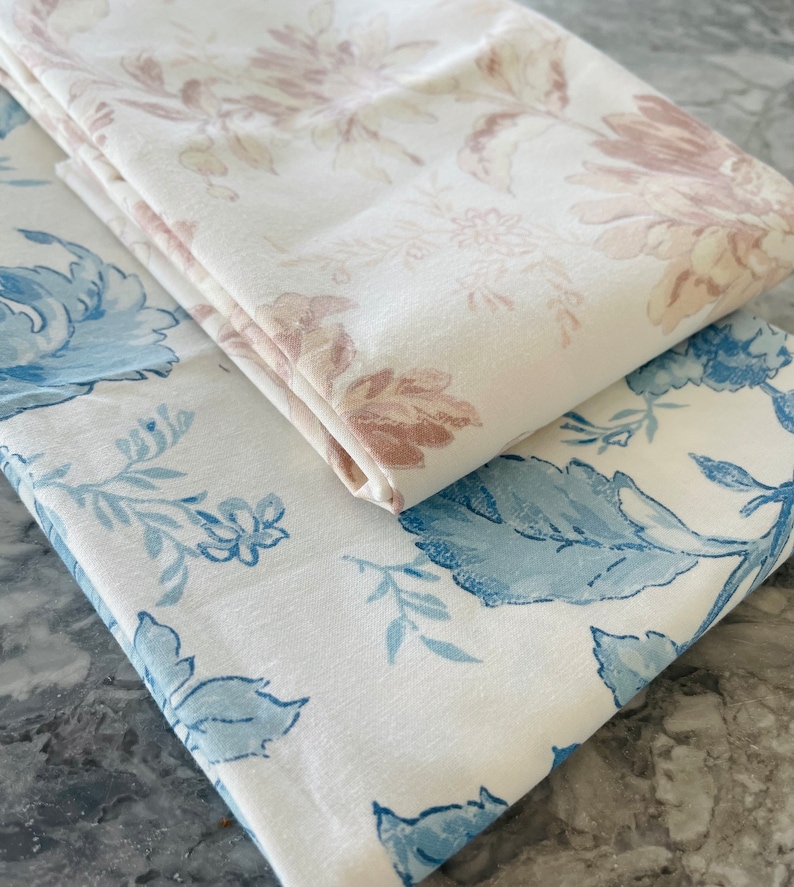 May include: Two pieces of white fabric with floral patterns. One fabric has a light pink floral pattern and the other has a blue floral pattern.