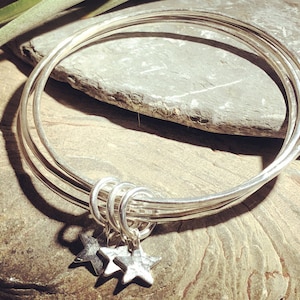 May include: A silver bangle bracelet with three stacked bands and two star charms hanging from the bottom.