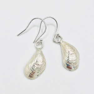 May include: A pair of silver dangle earrings featuring a detailed clam shell design.