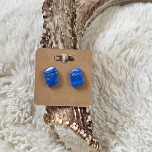 May include: A pair of blue and white marbled stud earrings on a brown earring display card. The earrings are rectangular with rounded edges. The display card is placed on a deer antler against a white, fluffy background.