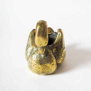 May include: A brass swan figurine with a detailed, textured surface. The swan is depicted with its head raised and wings folded, creating a small, open bowl shape. The brass has a warm, golden hue, and the overall design is compact and decorative.