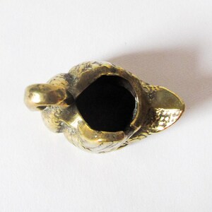 May include: A small, antique brass ashtray with a textured surface. The ashtray is shaped like a bird's head, with a deep, dark interior. The bird's beak forms the front of the ashtray, and the head is detailed with feathers.