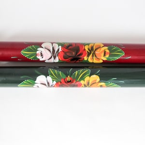 May include: Two wooden rolling pins. One is dark red with black handles and the other is dark green with red handles. Both are decorated with hand-painted floral designs in white, red, and yellow.