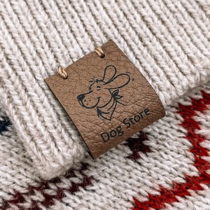May include: A brown leather patch with a cartoon dog wearing a bandana and the text "Dog Store" sewn onto a beige knitted fabric with red and blue stripes.