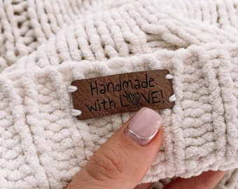 May include: A white crocheted blanket with a brown leather tag that says "Handmade with LOVE!" The tag has a small illustration of a ball of yarn and knitting needles.