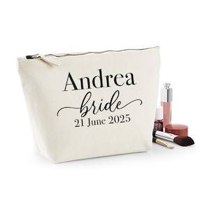 May include: A cream-colored cosmetic bag with a zipper closure. The bag is printed with the name "Andrea", the word "bride", and the date "21 June 2025" in black. Makeup items, including lip gloss and brushes, are next to the bag.