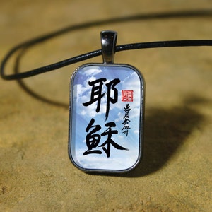 May include: A silver pendant necklace with a black leather cord. The pendant is a rectangular glass charm with a blue sky background and black Chinese calligraphy that reads "remarkable" in English. The charm also has a red seal with Chinese characters.